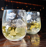Two glasses featuring silver leaf detailing with sparkling liquid in a low-level light scene.