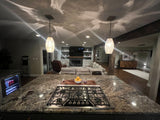 Modern kitchen with gas stove and granite countertop, open-plan living area in the background, all illuminated by two hand-blown glass pendant lights with a silver-leaf design.