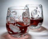 Two glasses featuring silver leaf detailing with red liquid on a gray background.