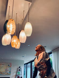Julie Conway, founder of LUMI Collection, looking up at modern oval-shaped pendant lights in a room with large windows.