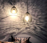 Two grey crackled glass pendants illuminating a speckled light effect on grey walls with the tops of ONDA pillows at the bottom left 