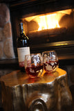 Two glasses on a wood coffee table with silver-leaf designing and speckles. Each glass hold red white and is next to a wine bottle in front of the fireplace.