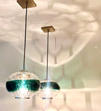 Two teal BOLA pendants hung in a white room with metal hexagon pattern-making lightbulb acessories.