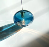 A recycled glass pendant light in blue color with a visible wiring and a reflective surface, set against a white background.