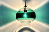 An oval/circular glass pendant in clear and teal, with light reflecting in a band of color.