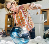 Julie Conway, the owner of Lumi Collection, holding an ocean blue BOLA pendant.
