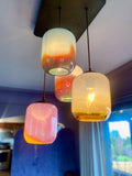 Four colorful glass pendant lights hanging from a ceiling with full and vibrant lights