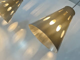 A modern perforated steel pendant light tilted at a 45 degree angle featuring a designs that cast patterned shadows and spotlights