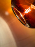 An amber colored BOLA glass pendant in the right hand corner of the picure, creating an auburn band of light on the wall.