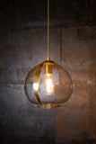 A clear sphere glass pendant light with a gold leaf detailing, hanging from a metal chain, completely aglow with a metal background