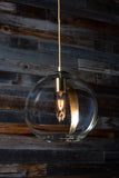 A clear sphere glass pendant light with a gold leaf detailing, hanging from a metal chain, and low lighting with a rustic wood background