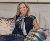 Julie Conway holding two square-shaped velvet throw pillow at her side with a geometric pattern featuring blue and orange light effects
