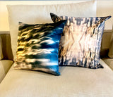 Two square-shaped velvet throw pillows with a geometric pattern featuring blue and orange light effects, on a couch