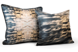 Two square-shaped silk throw pillows with a geometric pattern featuring blue and orange light effects, displayed on a white background