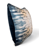 Side of a square-shaped velvet throw pillow with a geometric front pattern featuring blue and orange light effects and dark backside, displayed on a white background