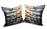Two square-shaped silk throw pillows with a geometric pattern featuring blue and orange light effects, displayed on a white background