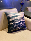 A square-shaped silk throw pillow with a geometric pattern featuring blue and orange light effects, displayed on a couch