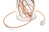 A close-up of the clear bottom of a SERAFINA lamp and its bundled copper cord