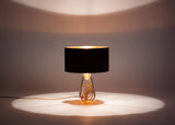 A modern lamp with a black top and glass bottom showcasing the copper cording within, turned fully on with lights that brighten the room.