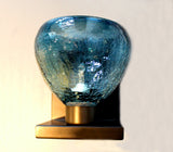 A wall-mounted sconce with a peacock soft blues coloring made of crackle glass on a bronze metal bracket.