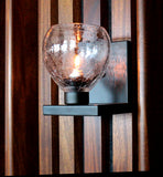 A wall-mounted clear glass crackle glass globe on a bent black metal bracket hanging on a wooden wall