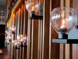 A scattered wooden beam wall with clear ACQUA sconces light layering across