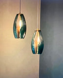 A pair of teal oval pendants that have a gold-colored precious metal contour stripe, used as an accessory for LUMI Collection's glass pendants.