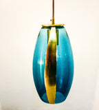 A close-up image of a gold-colored contour stripe on a gradient blue ELETTRA glass pendant on a white background