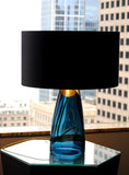 The blue glass varient of the SERAFINA lamp collection infront of a city window
