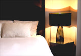 A bedroom scene with a modern grey glass lamp fully on.