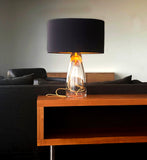 A statement piece lamp with a glass bottom base and a classy black circular top with gold color cording inside, all in a living room scene