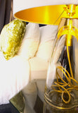 A white and gold lamp with clear glass in a bedroom scene.
